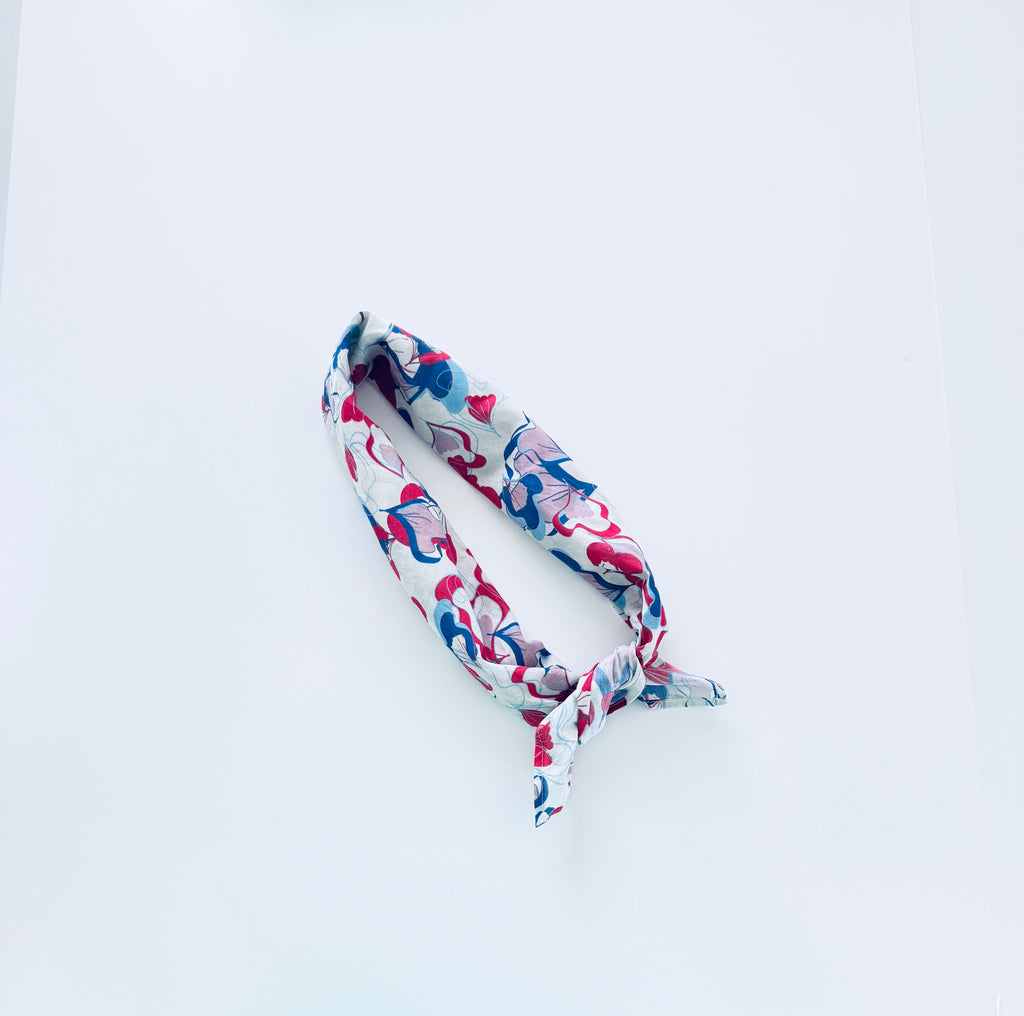 A cotton headband with a colorful abstract floral pattern in pink, blue, and red on a white background, tied in a knot and displayed on a clean white surface.