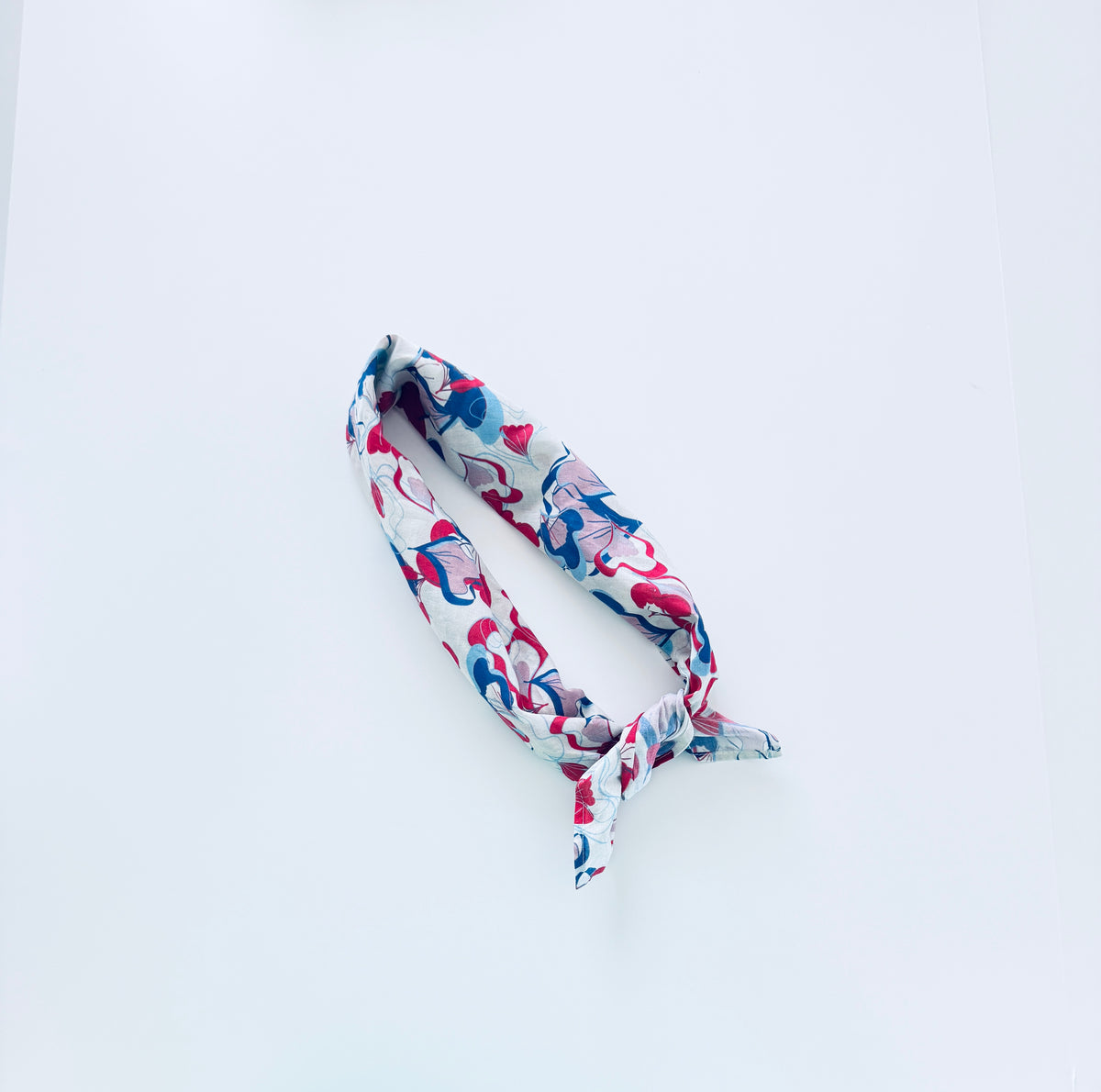 A cotton headband with a colorful abstract floral pattern in pink, blue, and red on a white background, tied in a knot and displayed on a clean white surface.