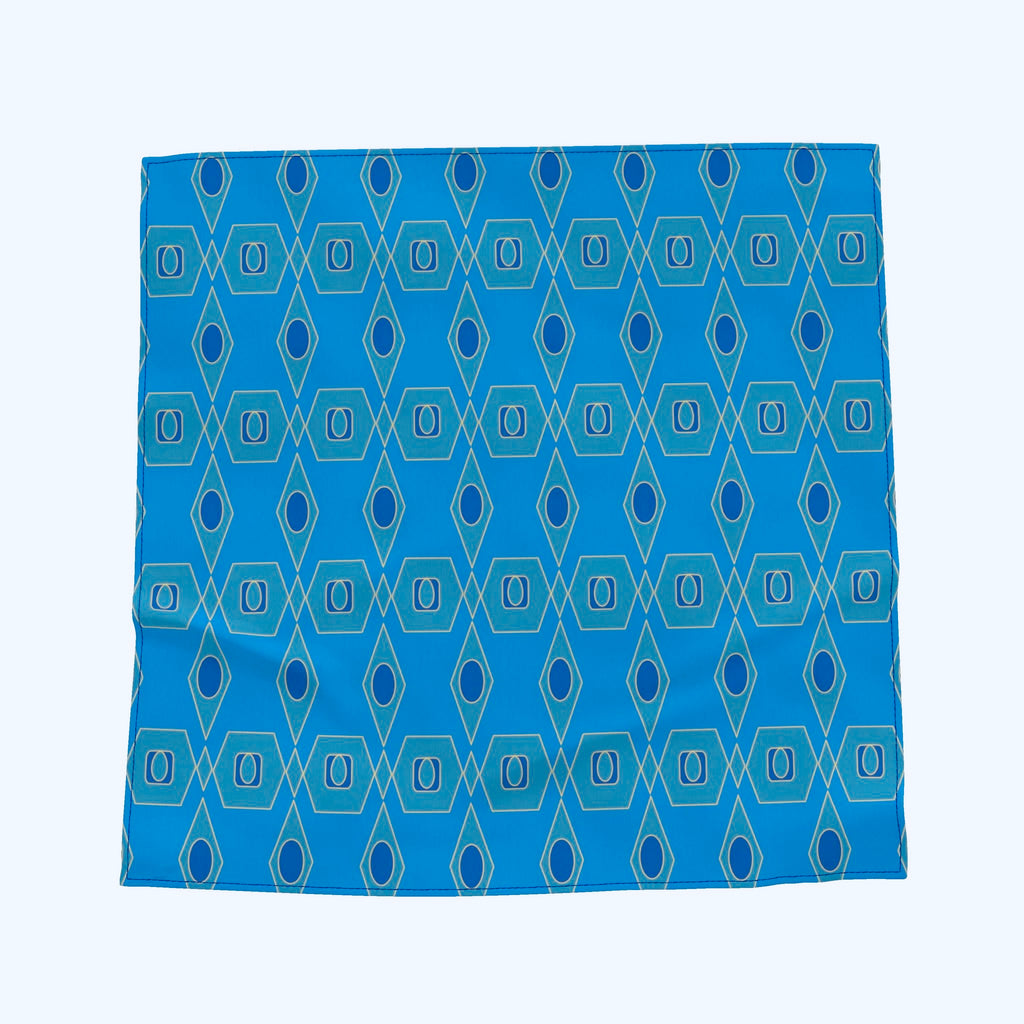 A square scarf with a geometric pattern of blue, teal, and light blue diamonds and ovals, laid flat against a white background.